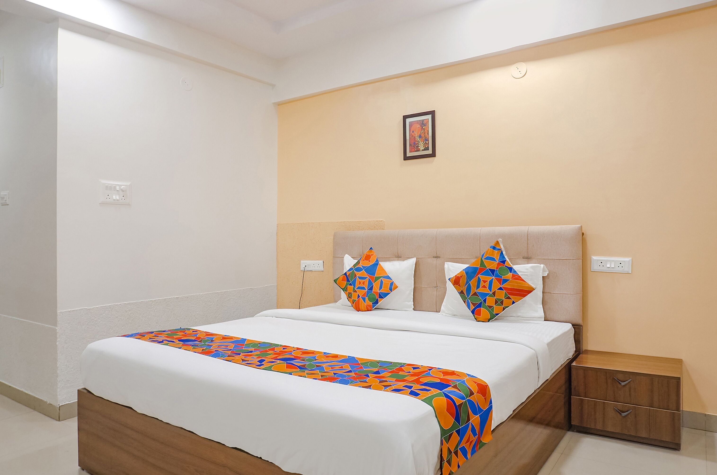 Quarto de hotel com cama, mesa de cabeceira e quadro na parede.