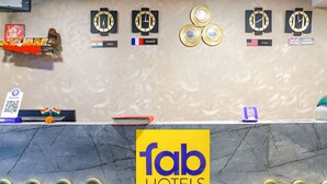 A reception desk with clocks displaying different countries, a Fab Hotels logo, and a QR code for a phone app. - FabHotel Embassy (Pune)