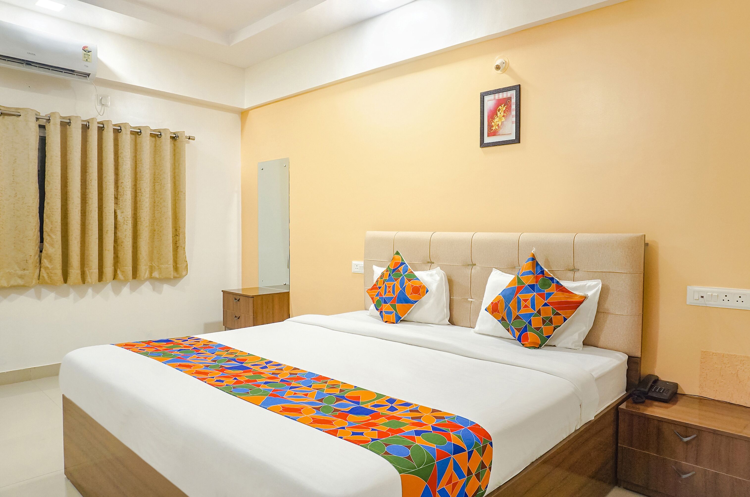 Una habitación de hotel con cama, mesita de noche, teléfono, espejo y aire acondicionado instalado en la pared.