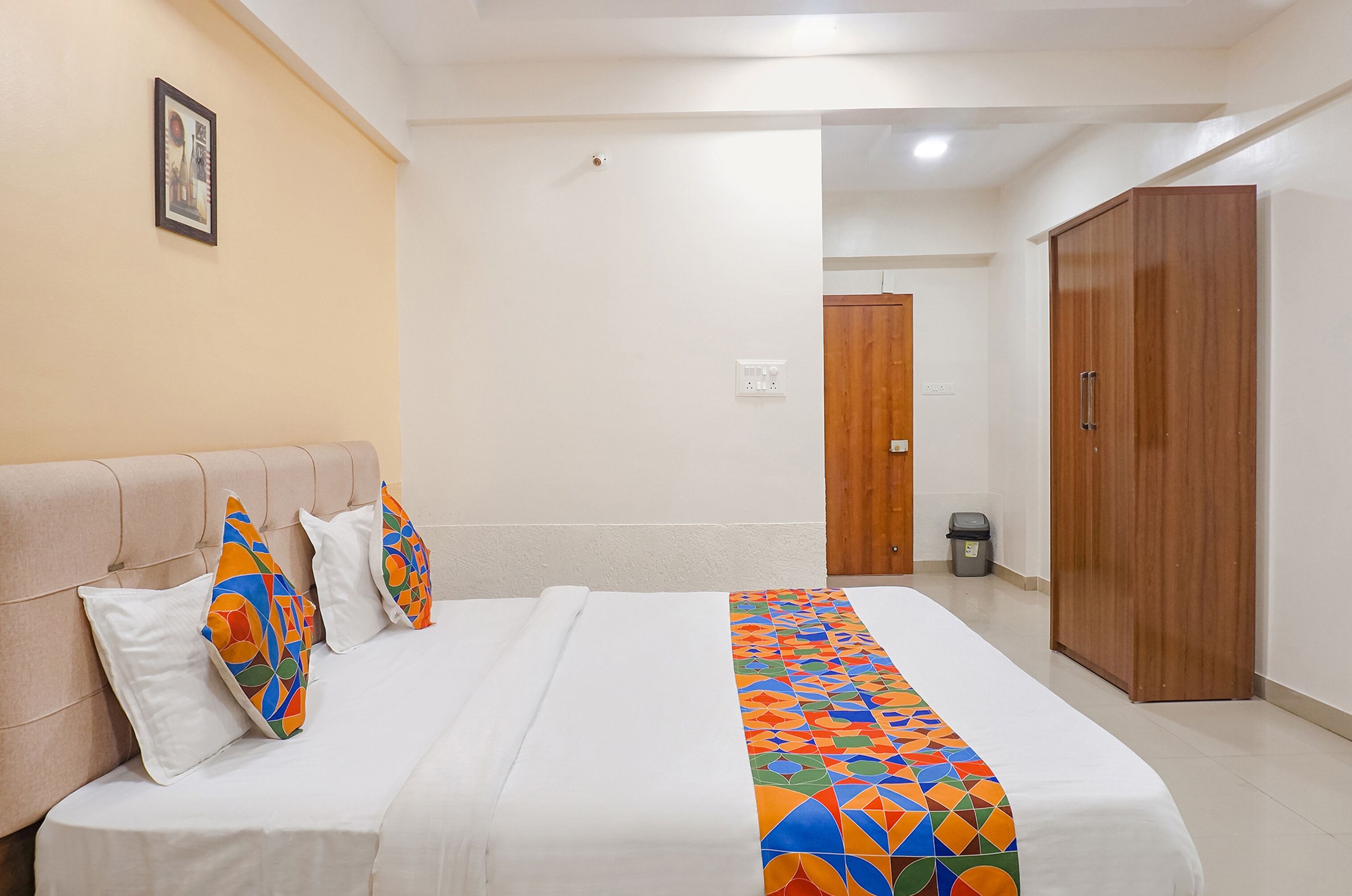 A neatly made bed with a colorful geometric-patterned bedspread, a beige headboard, and two decorative pillows.