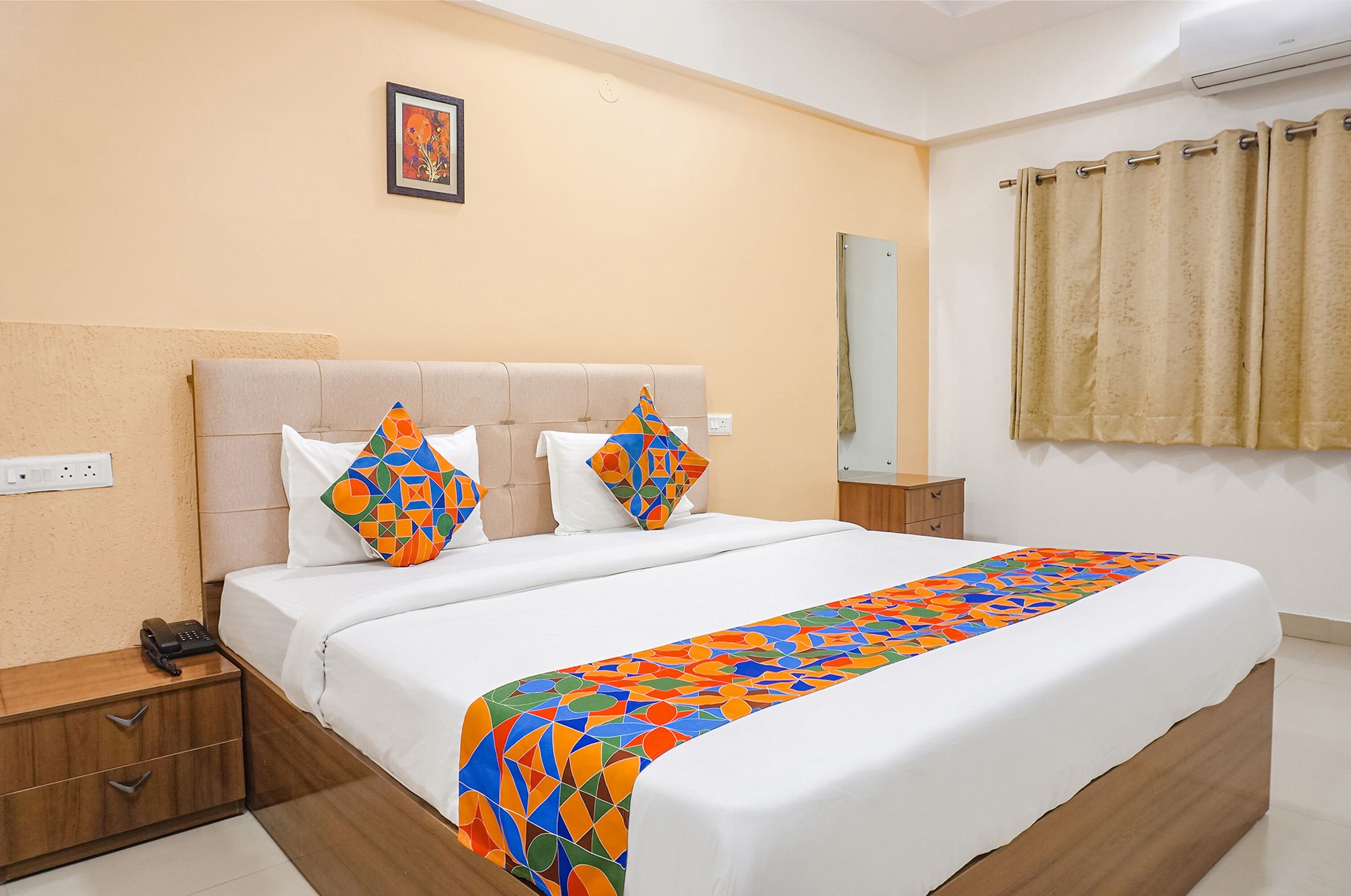 A neatly made bed with a colorful geometric-patterned bedspread, a headboard, and a bedside table with a phone.