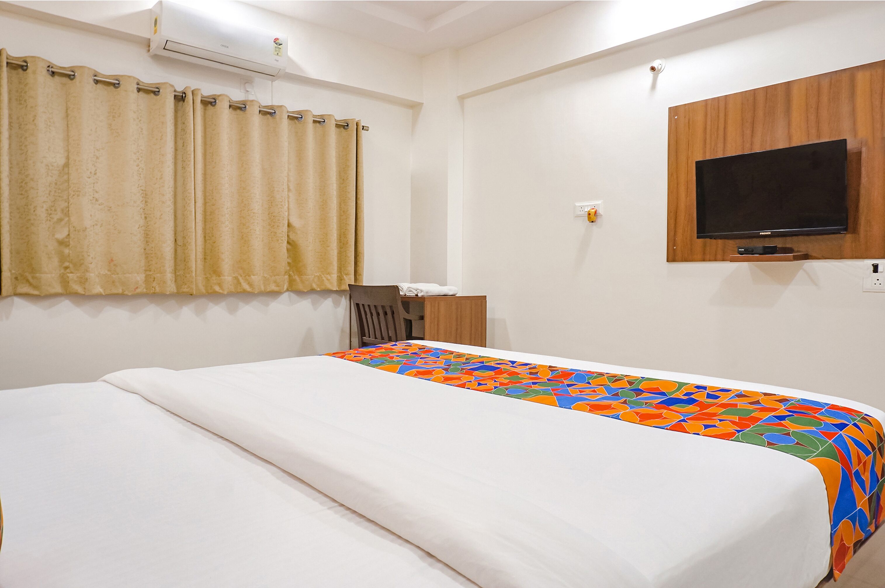 A hotel room with a bed, a TV mounted on the wall, and a window with curtains.
