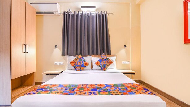 A hotel room with a bed, a nightstand, a wardrobe, and a window with curtains. - Fabhotel Saltel (Kolkata)