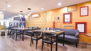 Un espace de restauration dans un hôtel, avec des tables et des chaises, un canapé et des tableaux encadrés au mur.