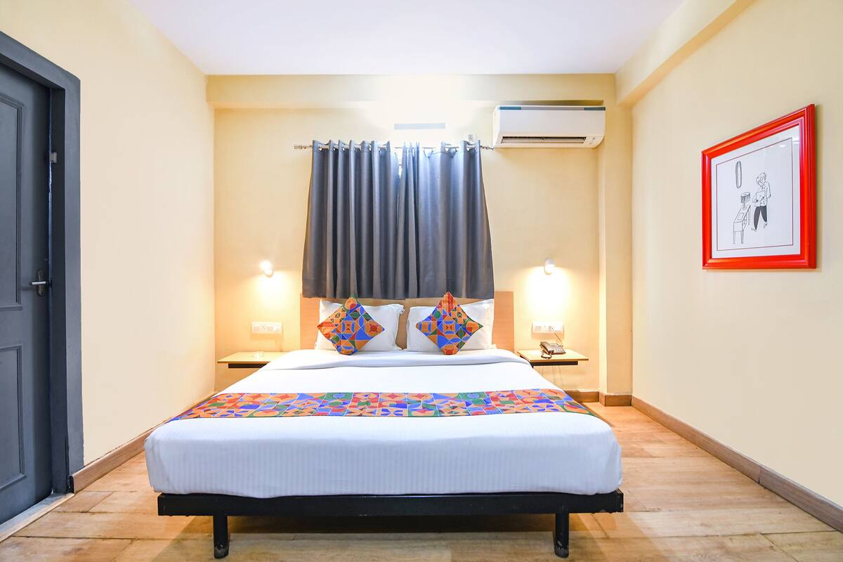 Habitación de hotel con cama, dos lámparas de noche, mesita de noche, un cuadro enmarcado en la pared y un equipo de aire acondicionado.