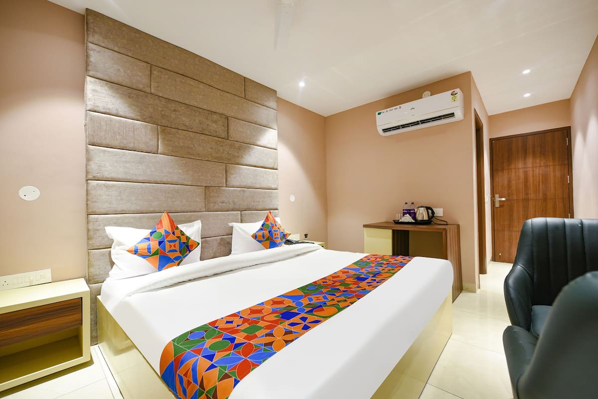 A modern hotel room with a large bed, a headboard, an air conditioning unit, a desk, and a chair.