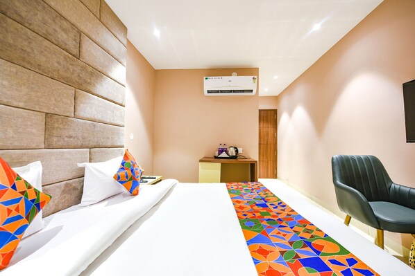 A hotel room with a bed, a desk, an air conditioner, and a chair.