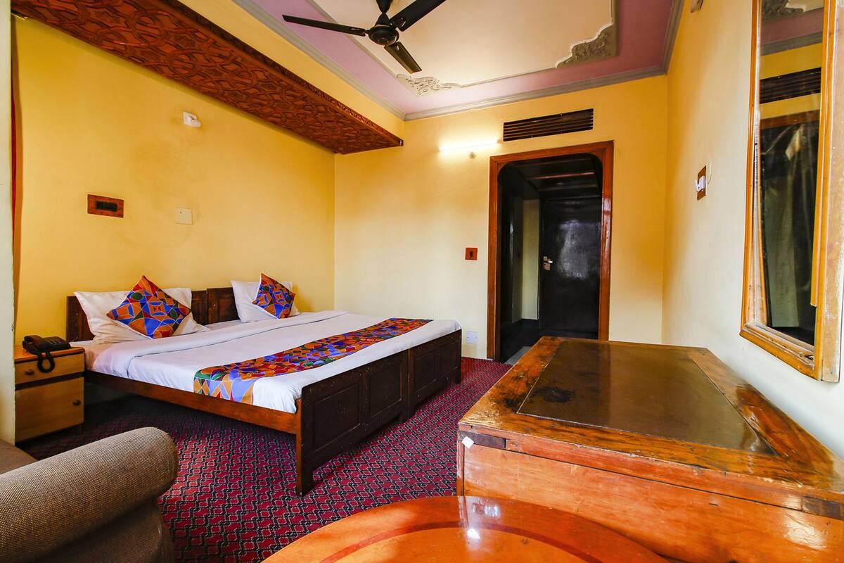 A hotel room with a bed, wooden nightstand, and a wooden table.