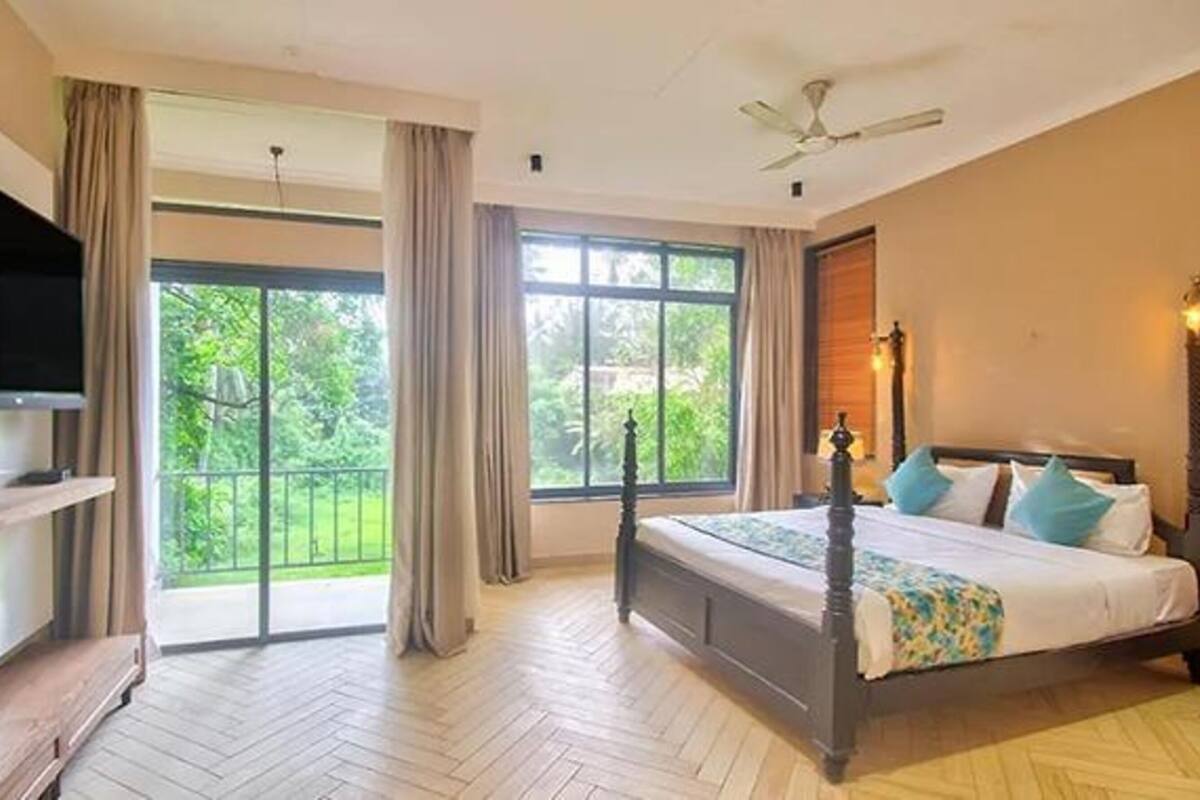 A bedroom with a large bed, a TV, and a balcony with curtains.