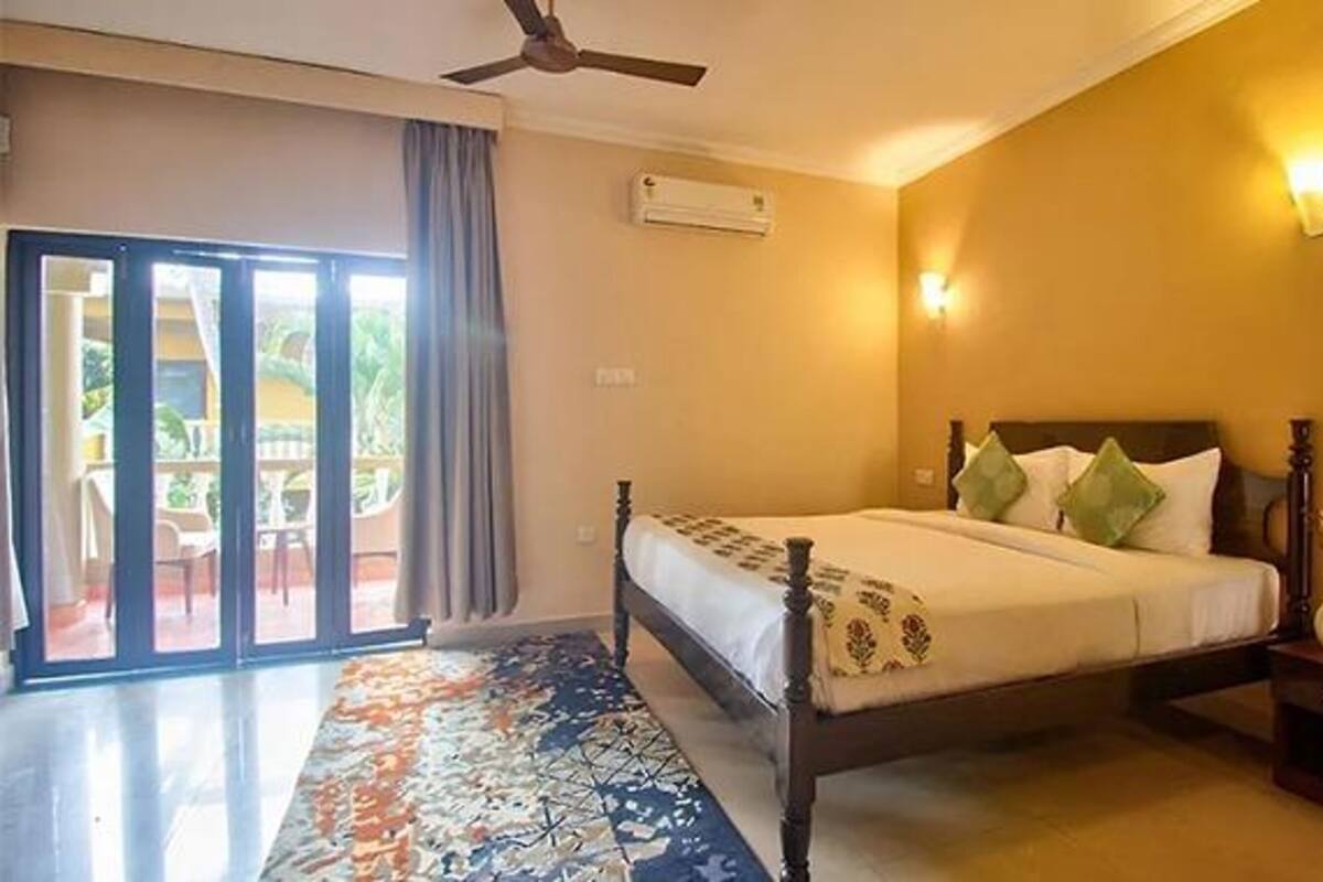 A bedroom with a bed, a ceiling fan, an air conditioning unit, a nightstand, and a view of the outside through a sliding door.