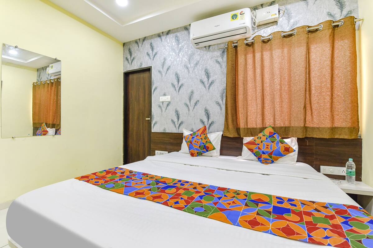 A hotel room with a bed, a nightstand, an air conditioning unit, and a window with curtains.