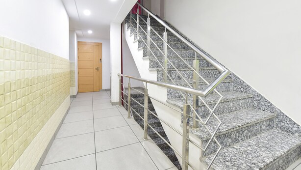 A hallway with a tiled floor, a staircase with metal railings, and a wooden door at the end. - Fabexpress Perfect (Samba)