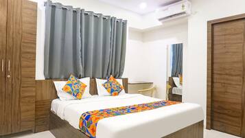 A bedroom with a bed, curtains, a wardrobe, a desk, and an air conditioning unit.