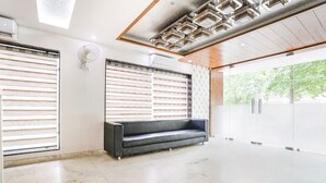 Una hall moderna con un divano in pelle nera, ampie finestre con tende e un soffitto a motivi geometrici.