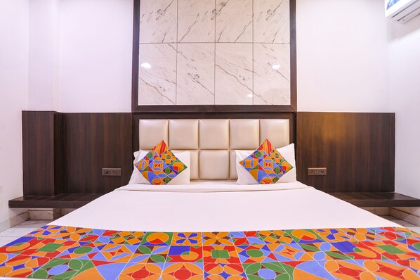 Una habitación de hotel con una cama grande, cabecera de mármol y un tapete de diseño geométrico y colores vivos.