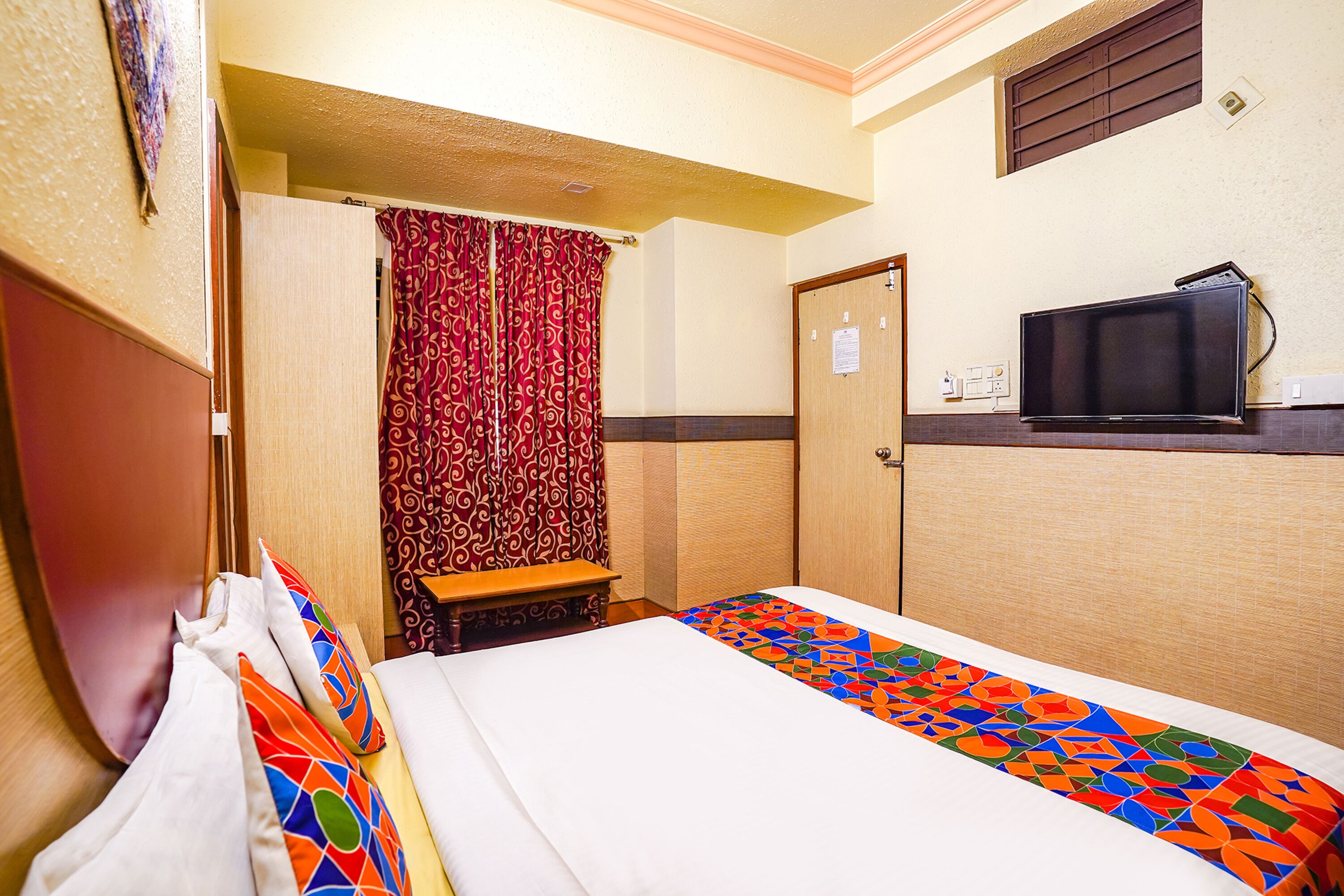 A hotel room with a bed, a television, a door, and a patterned curtain.