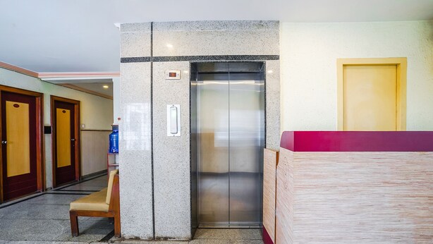 Een hotel lobby met een lift, receptiebalie en een bank.