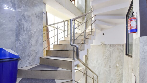 A staircase with metal railings, marble walls, and a blue trash bin. - Fabexpress Glacier Inn (Jammu)