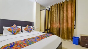 A hotel room with a bed, a nightstand, a blue trash bin, and a wardrobe. - Fabexpress Glacier Inn (Jammu)