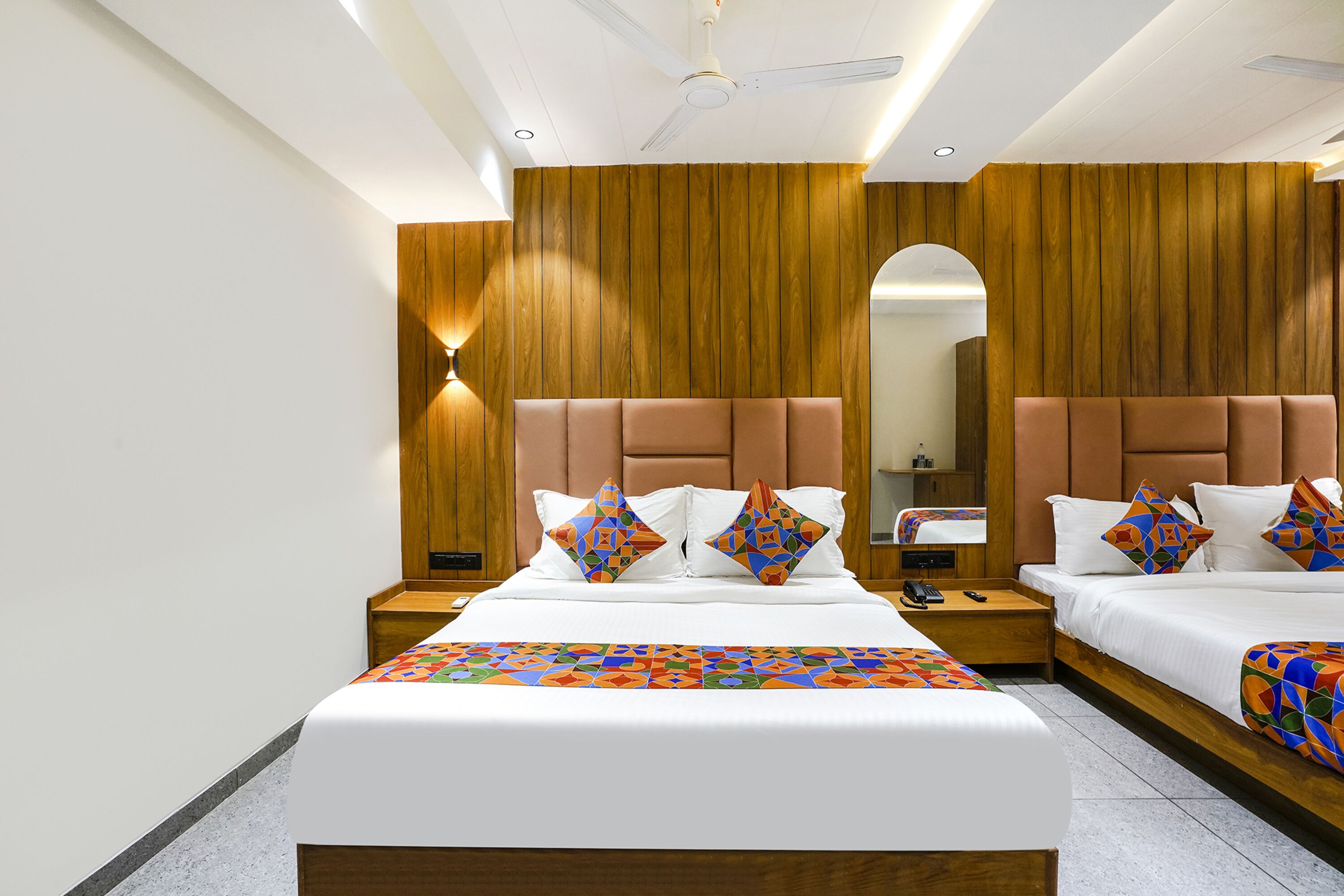 Habitación de hotel con dos camas, paneles de madera, ventilador de techo y un espejo grande.