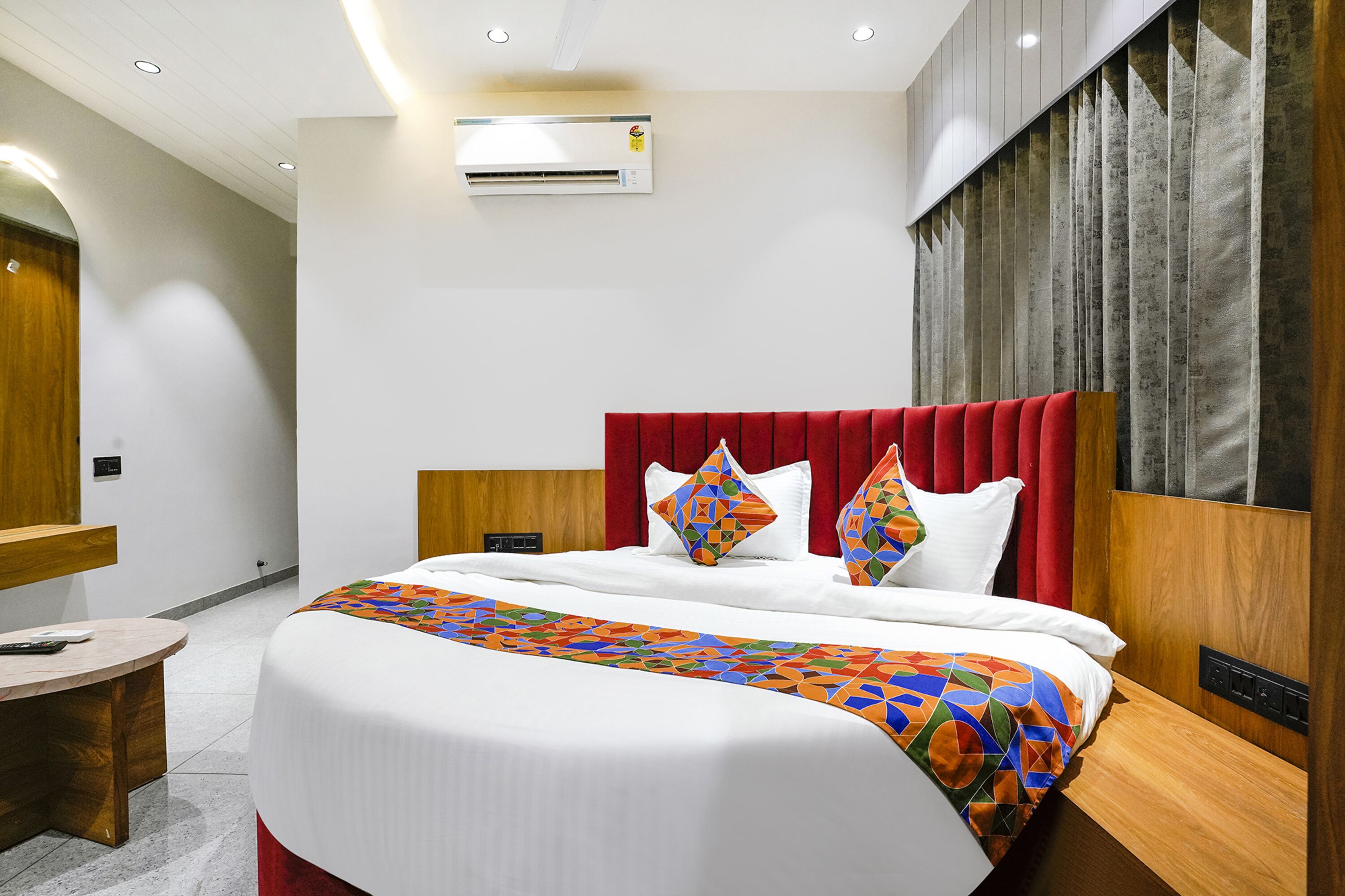 Une chambre d’hôtel avec un grand lit, une tête de lit en bois, un mur d’accent rouge et un système de climatisation moderne.