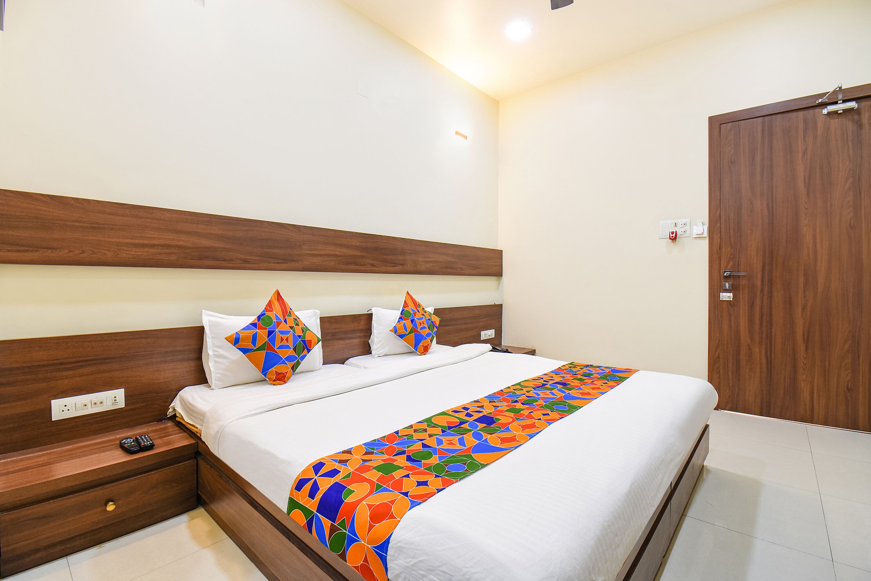 A neatly made bed with a colorful blanket, a wooden headboard, and a nightstand with a remote control.