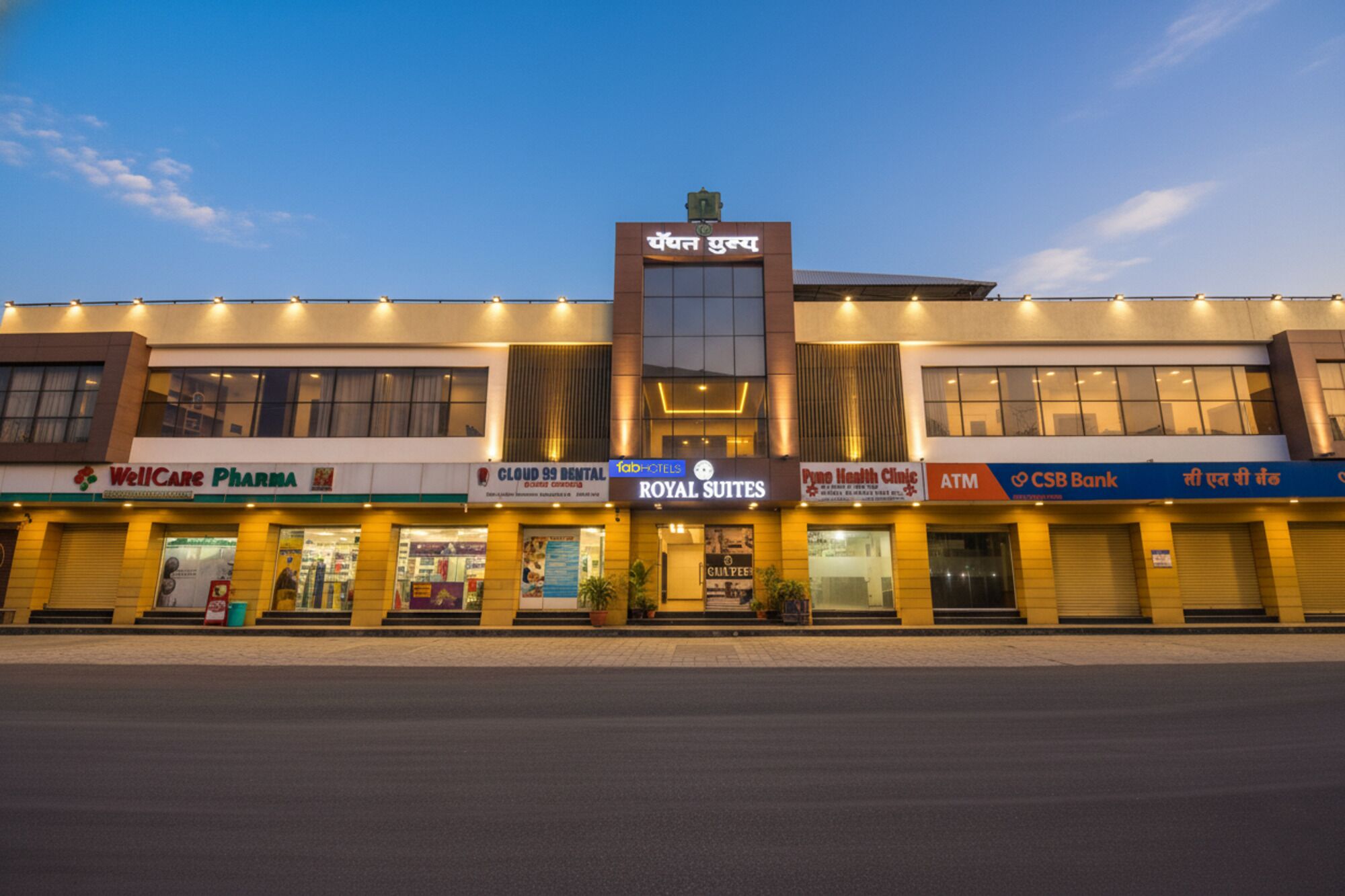 A hotel with a sign reading "Royal Suites" and various amenities including a WellCare Pharmacy, Cloud 99 Dental, FabHotels, and a CSB Bank ATM.