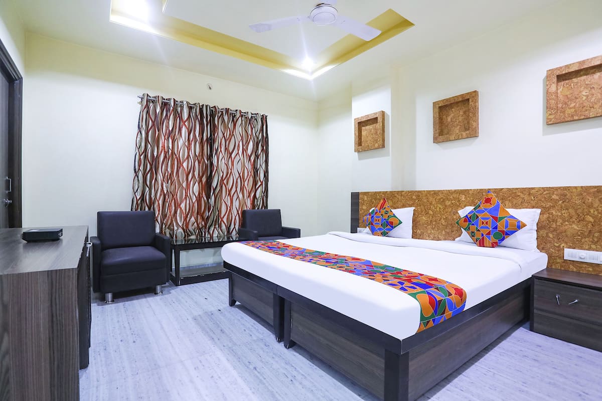 A hotel room with a bed, a desk, a chair, a ceiling fan, and a window with curtains.