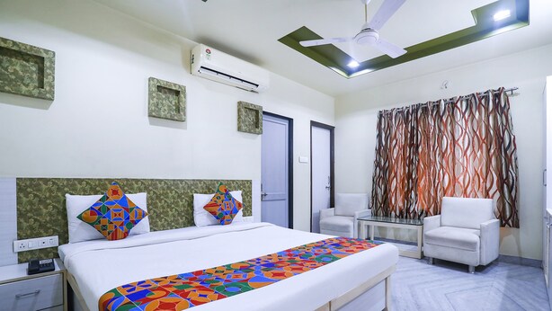 A hotel room with a bed, bedside tables, a chair, an air conditioning unit, and a curtain. - Fabhotel Gayatri Inn Annex (Nagpur)