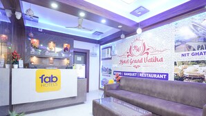 A hotel reception area with a reception desk, a sofa, and a potted plant. - Fabhotel Grand Vatika (Danapur)