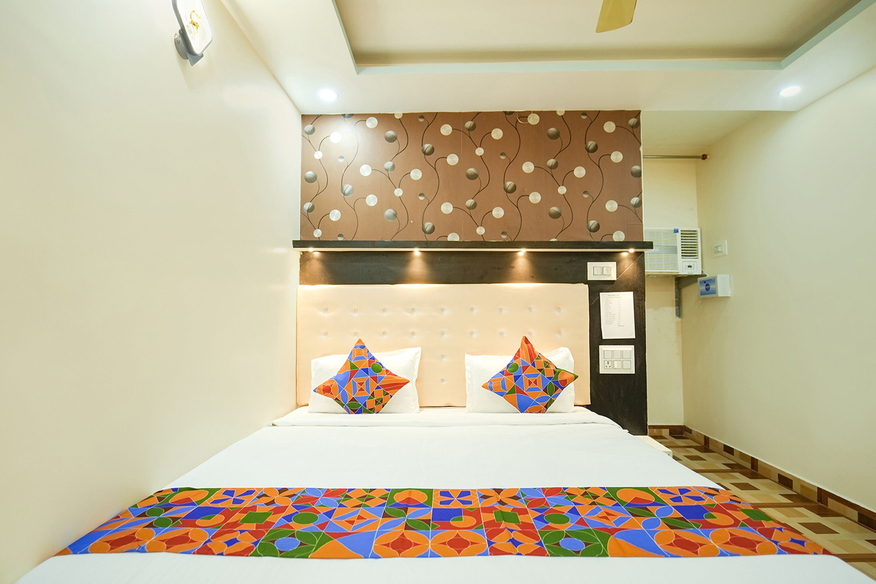 Une chambre d’hôtel avec un lit, une tête de lit à motifs et un climatiseur fixé au mur.