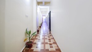 A long, narrow hallway with white walls and a patterned floor. There are potted plants along one side of the hallway. - Fabhotel Grand Vatika (Danapur)