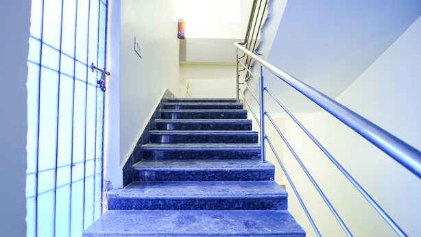 A staircase with blue steps and metal railings, leading to a landing with a door and a small plant. - Fabhotel Grand Vatika (Danapur)