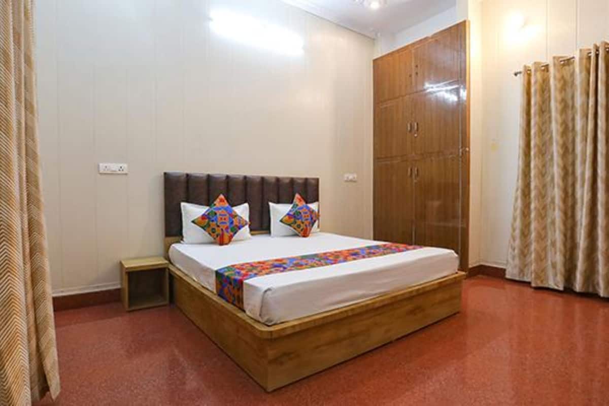 A bedroom with a wooden bed, two pillows, a nightstand, a wardrobe, and curtains.