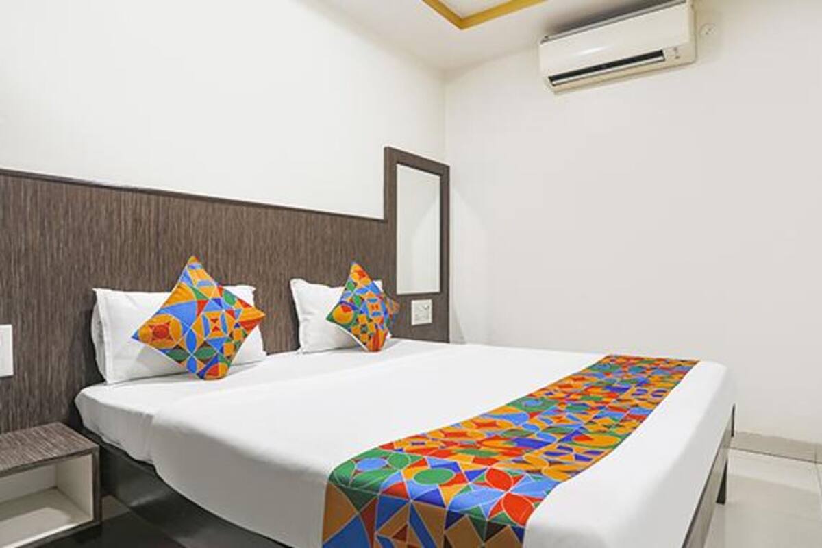 A hotel room with a bed, two pillows, a bedside table, and a wall-mounted air conditioner.