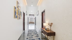 A hallway with a patterned carpet, framed artwork on the walls, and a desk with a lamp and books. - Fabhotel Arjun (Nagpur)