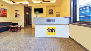 Zona de recepción de un hotel con mostrador de recepción identificado como 'Reception', un sofá, una mesa de centro, ventiladores de techo y un ventanal grande.
