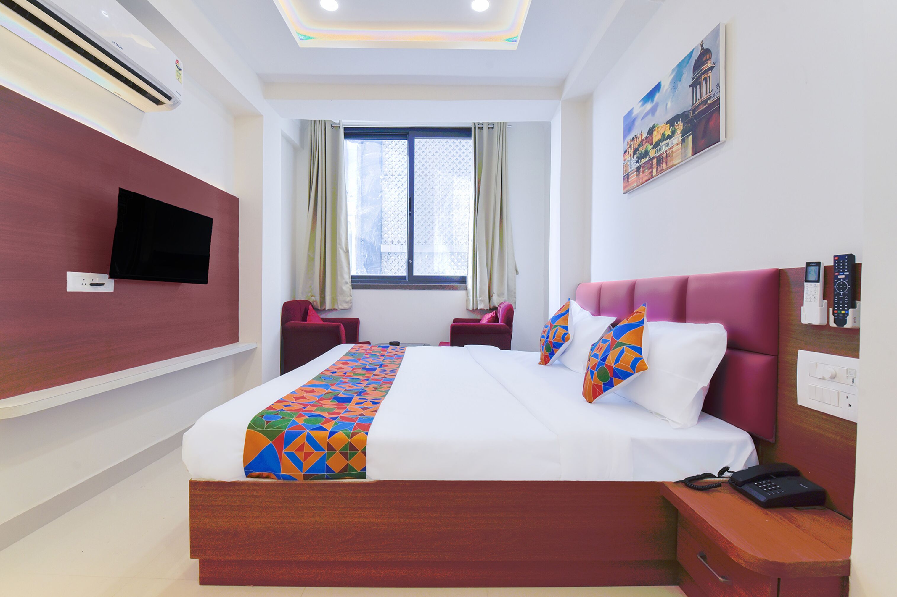 A hotel room with a large bed, a flat-screen TV mounted on the wall, a window with curtains, and a painting on the wall.