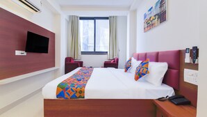 Habitación de hotel con una cama grande, un televisor de pantalla plana montado en la pared, una ventana con cortinas y un cuadro en la pared.