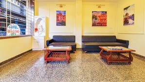 Un hall de hotel con dos sofás negros, una mesa de centro de madera y un mostrador de recepción.