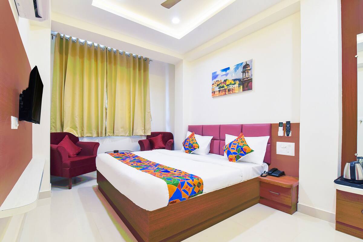 A hotel room with a large bed, a red sofa, a painting on the wall, and a ceiling fan.