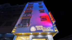 Un hotel llamado 'Hotel Samrat Regency' con un letrero llamativo, unidades de aire acondicionado y una entrada visible.