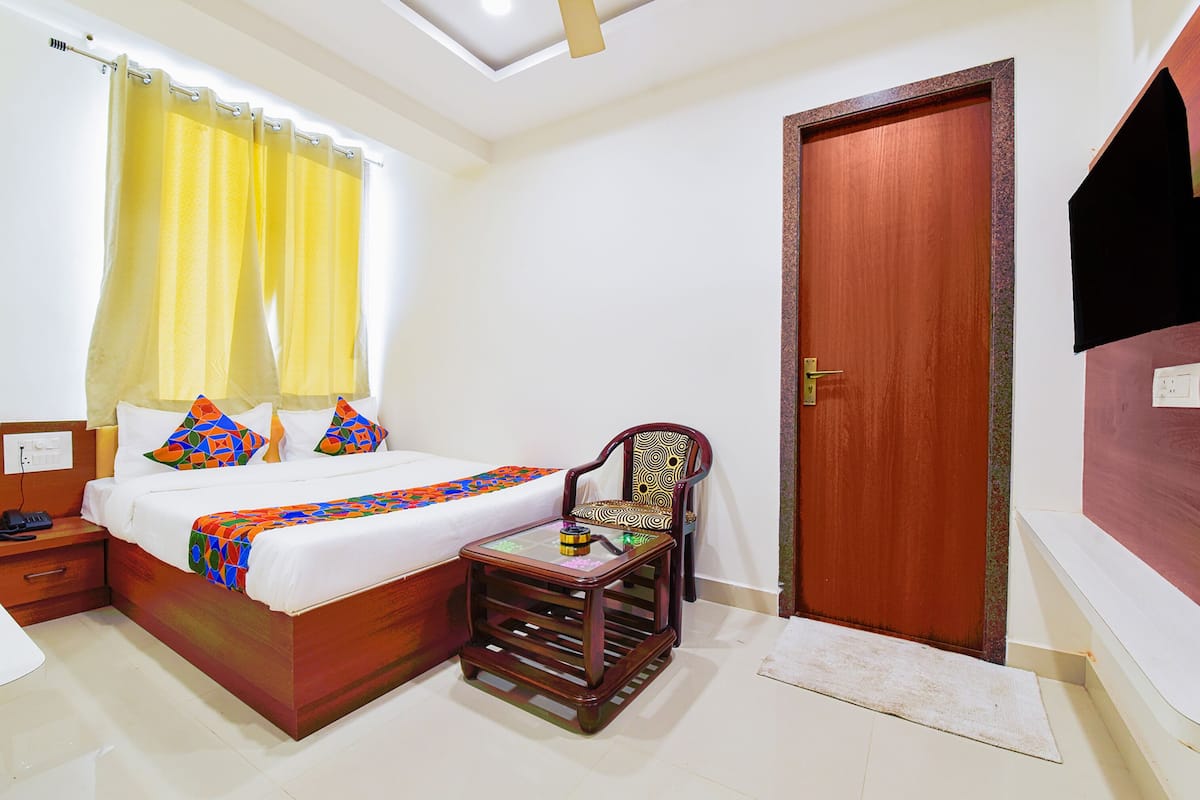 A hotel room with a bed, a chair, a small table, a wooden door, and a window with curtains.