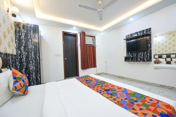 A hotel room with a bed, a ceiling fan, a TV mounted on the wall, and a patterned rug.