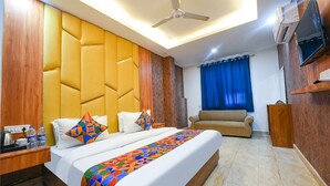 A hotel room with a large bed, a sofa, a TV, and a ceiling fan. - Fabhotel Grand Villa (New Delhi)