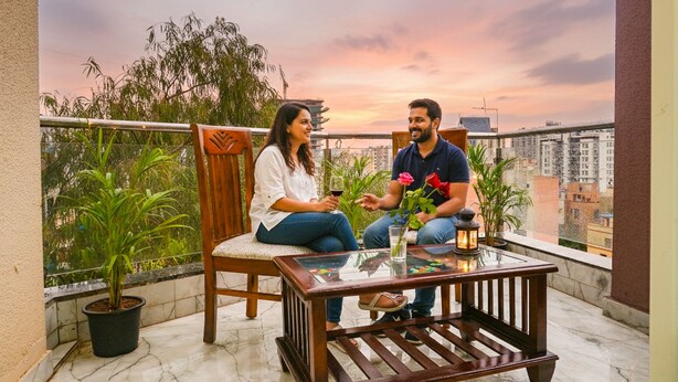 A couple sitting on a balcony with a city view, a glass table, and potted plants. - Fabhotel Falcon Executive (Pune)