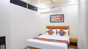 A hotel room with a bed, a nightstand, a chair, an air conditioner, and a ceiling fan. - Fabhotel Falcon Executive (Pune)