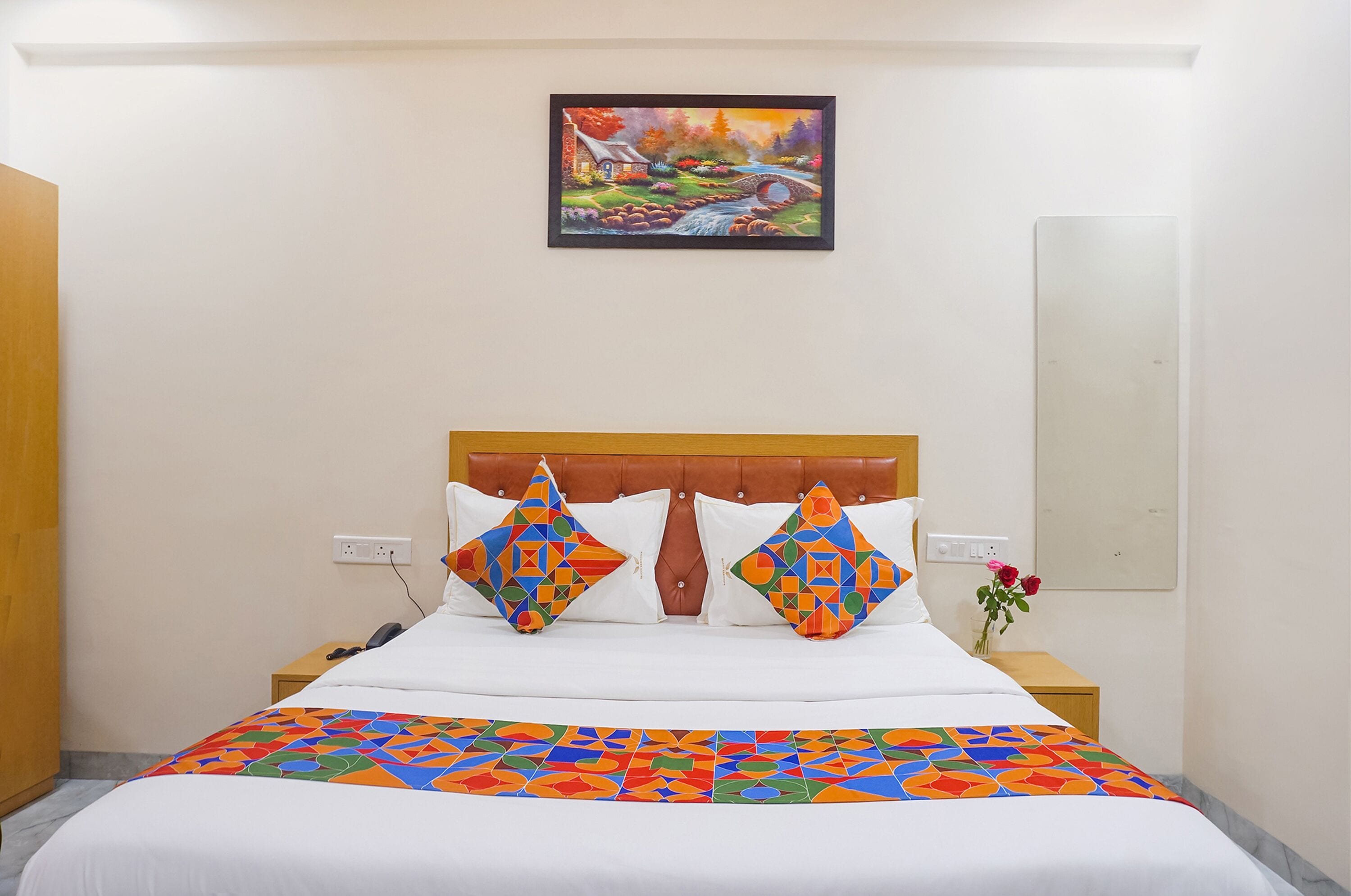 Una habitación de hotel con una cama, una mesita de noche, un cuadro en la pared y un espejo.
