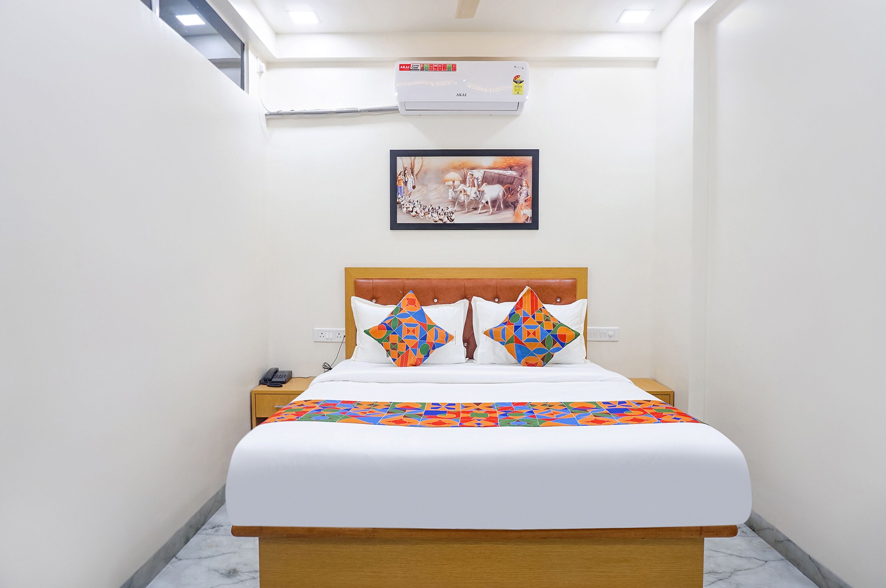 Une chambre d’hôtel avec un lit, une table de chevet, un téléphone et un tableau accroché au mur.