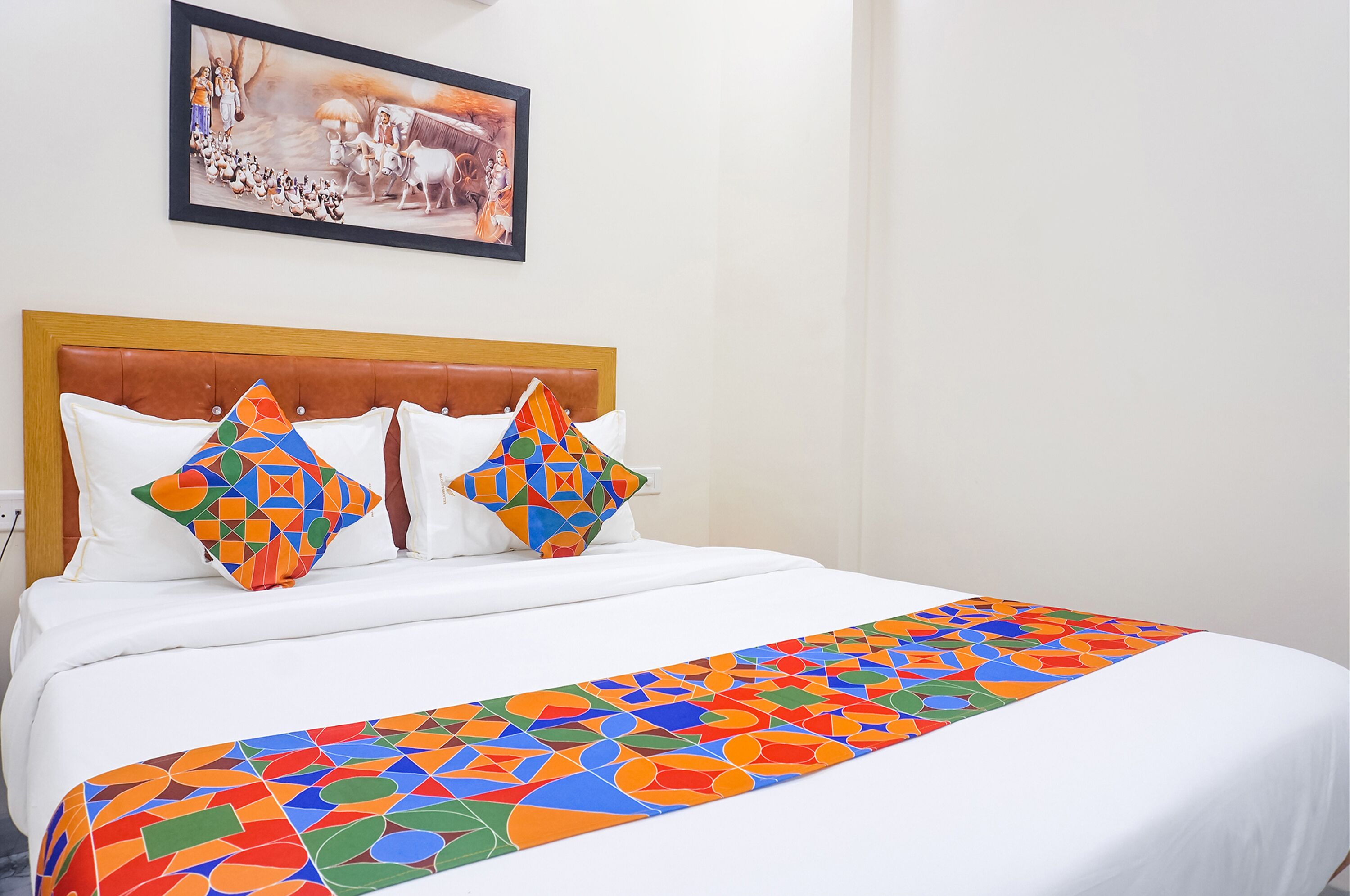 A neatly made bed with a colorful geometric-patterned bedspread and pillows, a framed picture on the wall, and a wooden headboard.